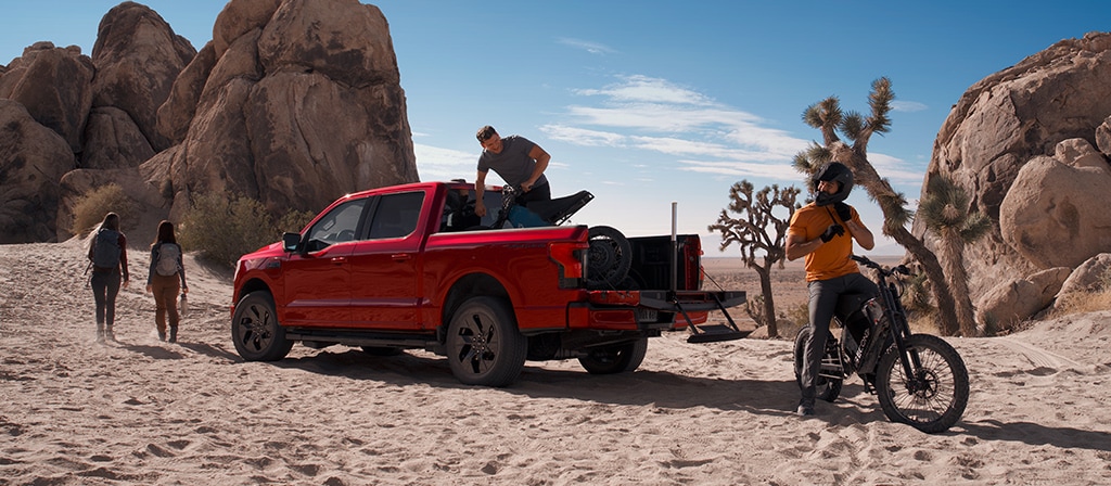 2025 Ford F-150® Lightning® pickup in the desert, with a dirtbike in the bed and one already unloaded