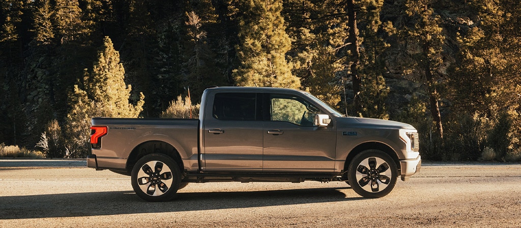 A 2025 Ford F-150® Lightning® in Iconic Silver parked on a paved road showing off the side profile