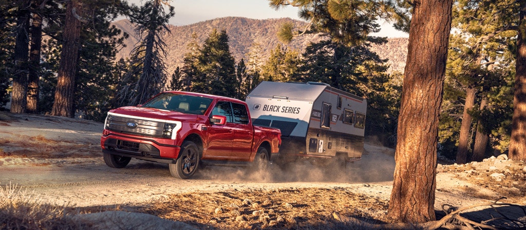 A 2025 Ford F-150® Lightning® hauling a camper on a dirt road in a scenic location