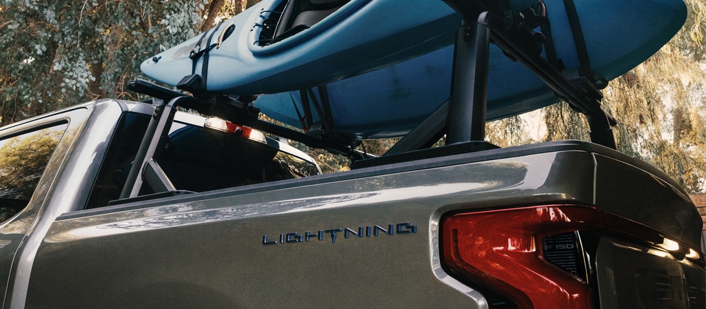 A 2025 Ford F-150® Lightning® is parked in a scenic location with kayaks in the truck bed
