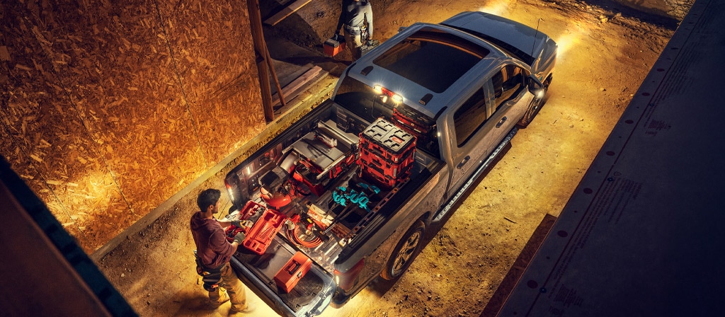 A 2025 Ford F-150® Lightning® lit up at night with a person on a construction site grabbing gear from the truck bed