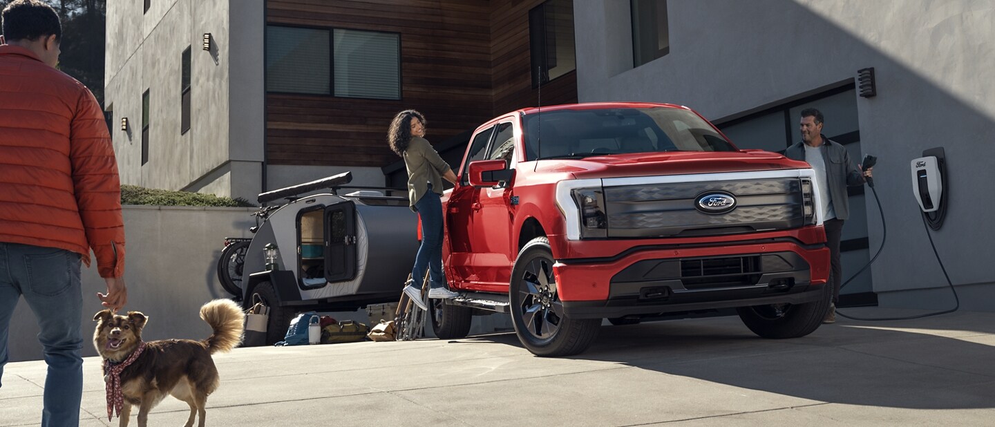 A red 2024 Ford® F-150 Lightning® pickup truck parked in the driveway of a large home